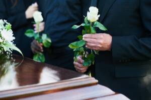 Gesto di omaggio: persone davanti al feretro, con di fiori bianchi tra le mani.