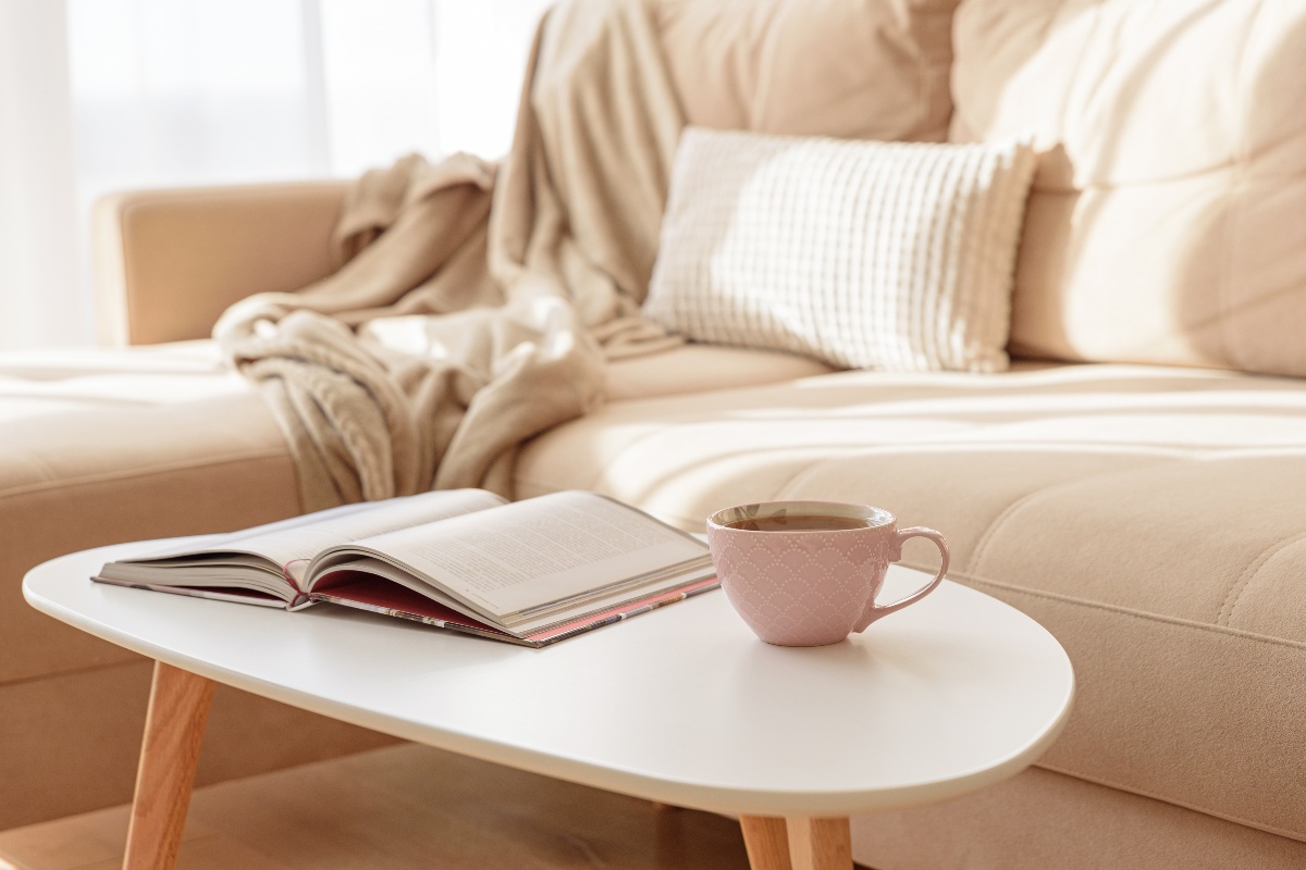 Un angolo accogliente con una tazza fumante e un libro appoggiati su un tavolino accanto al divano.