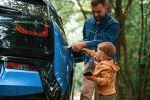 Un padre e suo figlio insieme mentre collegano il cavo di ricarica a un'auto elettrica.