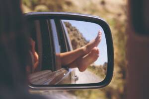 Lo specchietto laterale di un'auto cattura il riflesso di un passeggero che si gode il viaggio con i piedi fuori dal finestrino.